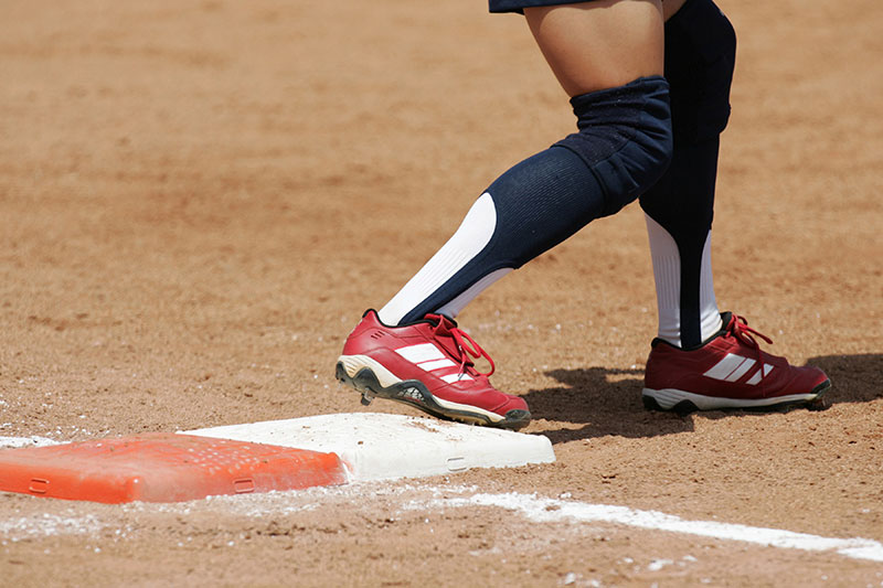 Girl on base wearing rubber molded softball cleats.