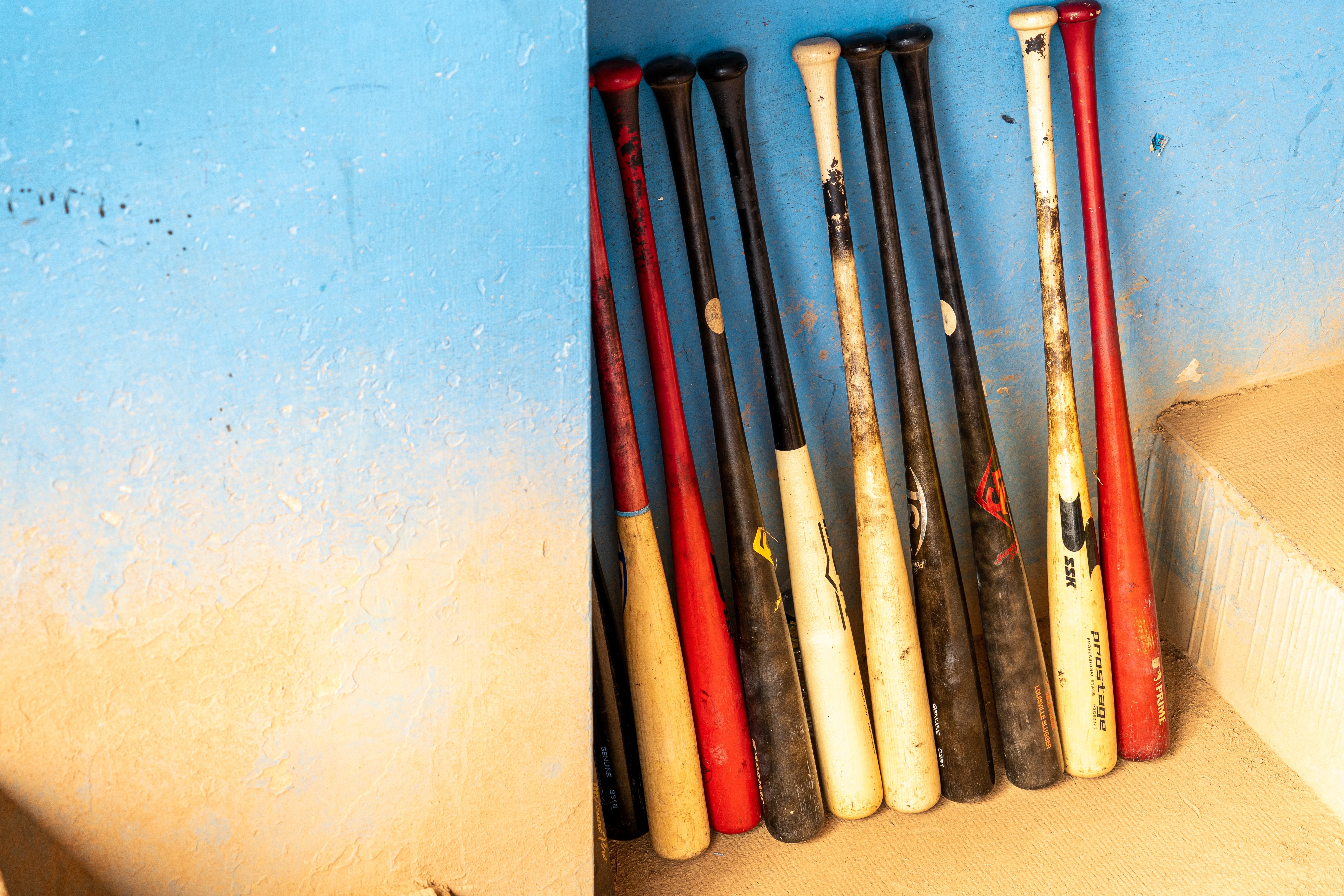 A large group of wooden bats leaning against a dugout wall.