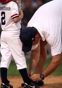 A coach tying a youth players baseball shoe.